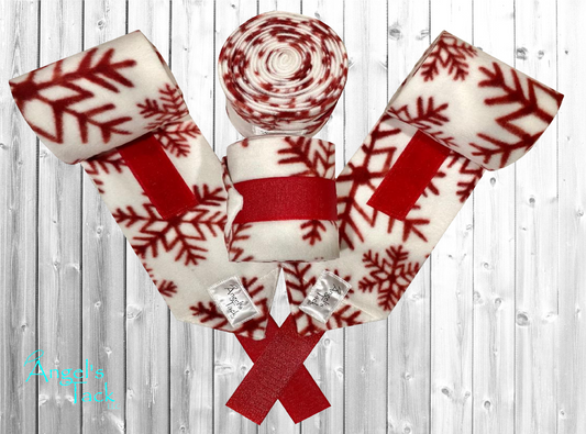 White horse polo wraps with red snowflake pattern by Angel's Tack LLC. Shown on a grey wooden background.